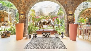 A stone-walled lobby with a central sculpture, patterned rugs, and potted plants. - Aroma Plaza Boutique Hotel (Cap Malheureux)