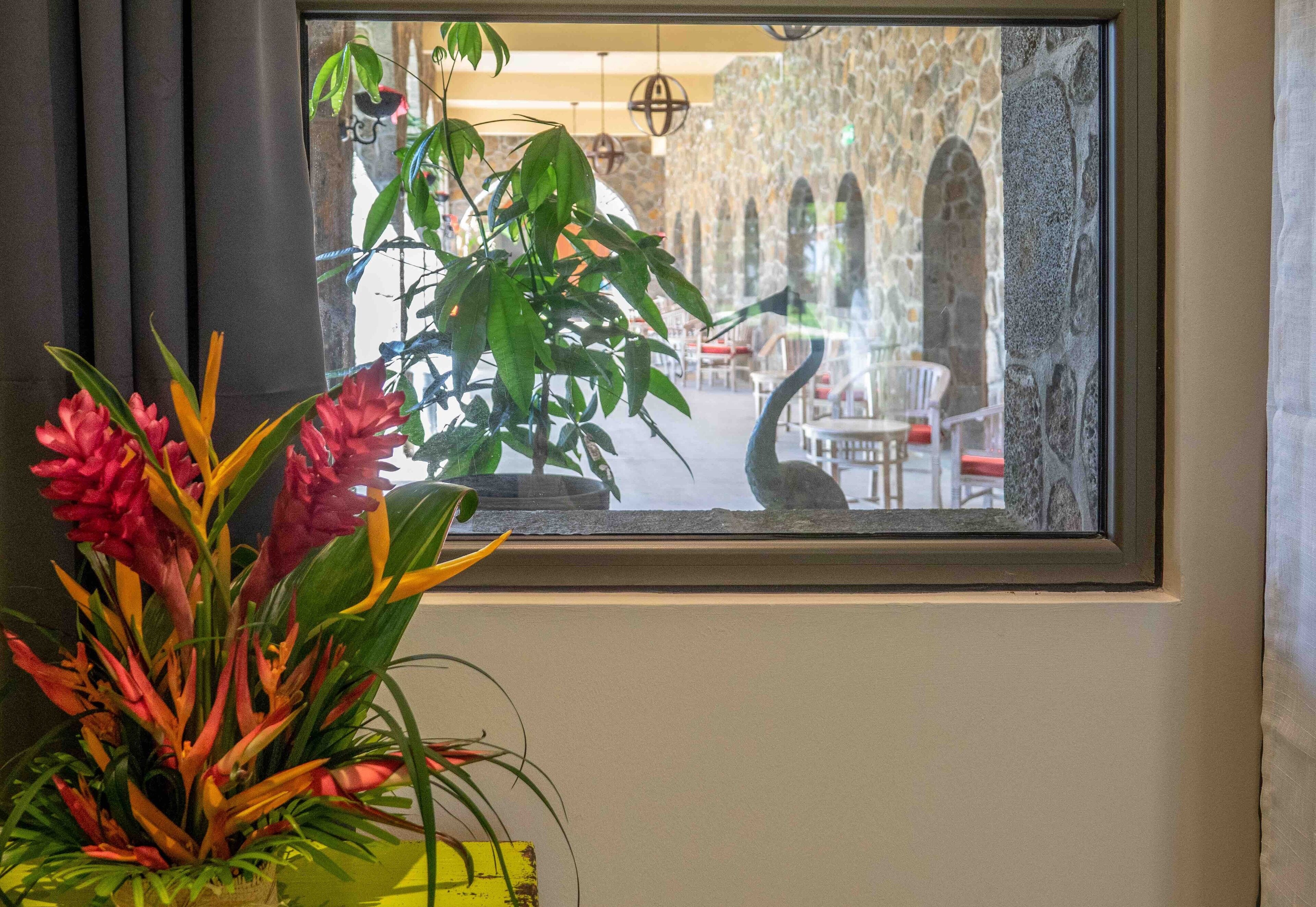 Una ventana con vista a un espacio interior que presenta una pared de piedra, arcos y luces colgantes.