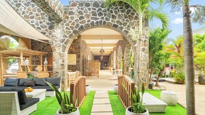 A stone archway leading to a lounge area with a sofa, potted plants, and a pathway. - Aroma Plaza Boutique Hotel (Cap Malheureux)