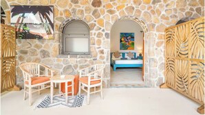 A stone-walled room with a bed, a TV, and a dining area with chairs and a table. - Aroma Plaza Boutique Hotel (Cap Malheureux)