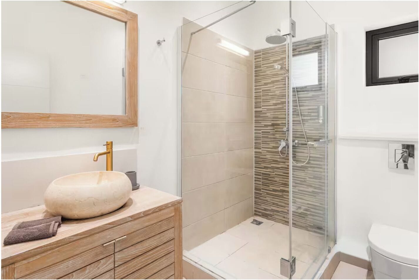 A bathroom with a wooden vanity, a round sink, a glass shower enclosure, and a toilet.