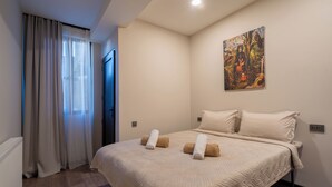 A hotel room with a large bed, beige bedding, a painting on the wall, and a window with curtains. - Niabi 4BDR Apartments with billiards  (Tbilisi)