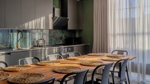 A modern kitchen with a wooden dining table, grey cabinets, and a large window with sheer curtains. - Niabi 4BDR Apartments with billiards  (Tbilisi)