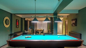 A pool table with a blue felt surface, surrounded by a dining area with chairs and a table. - Niabi 4BDR Apartments with billiards  (Tbilisi)