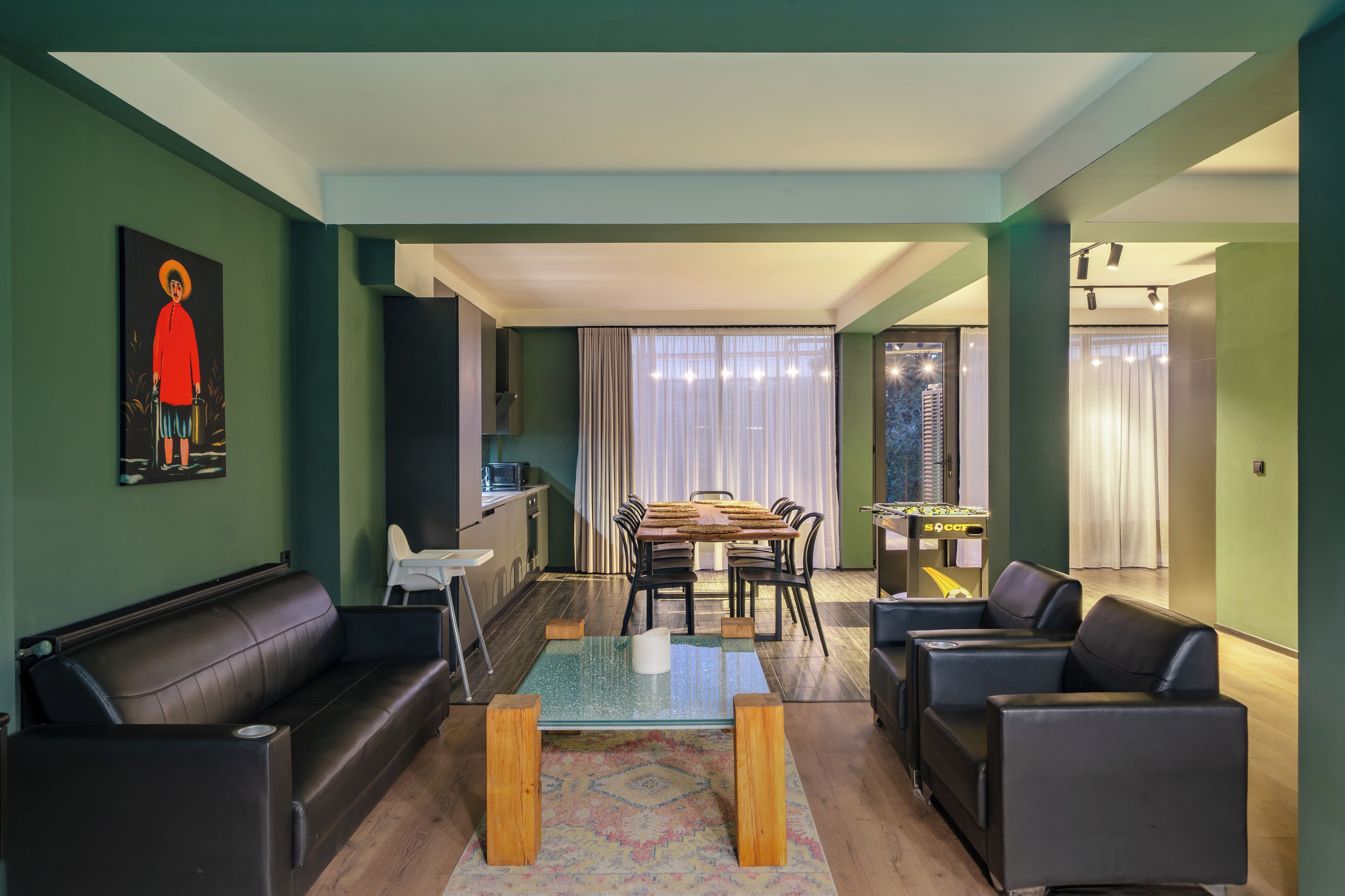 A modern living room with a glass coffee table, leather sofas, a dining area with a wooden table and chairs, and a kitchen in the background.