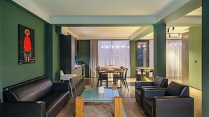 A modern living room with a glass coffee table, leather sofas, a dining area with a wooden table and chairs, and a kitchen in the background. - Niabi 4BDR Apartments with billiards  (Tbilisi)