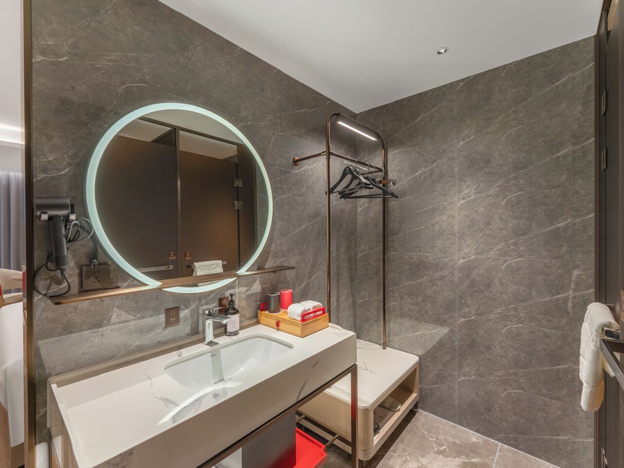 Een moderne badkamer met een ruime wastafel, een ronde spiegel en een handdoekrek.