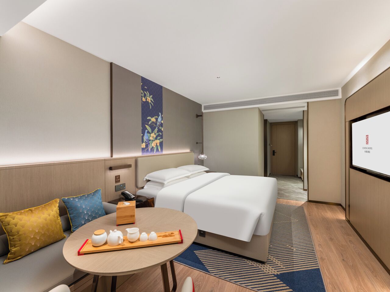A modern hotel room with a bed, a round table with tea set, a sofa, and a large painting on the wall.
