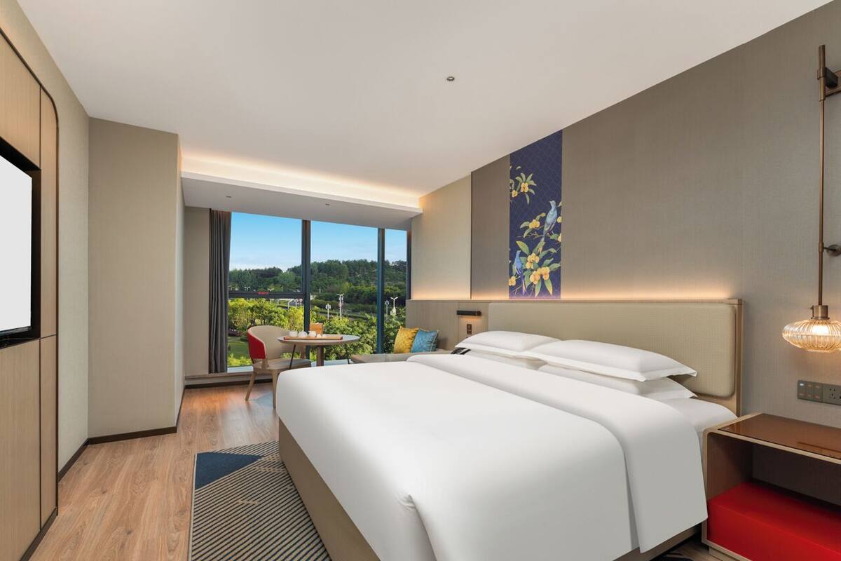 Een moderne hotelkamer met een groot bed, een bureau, een stoel en uitzicht op het landschap.