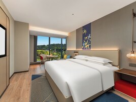 Habitación de hotel moderna con una cama grande, un escritorio, una silla y vistas al exterior.