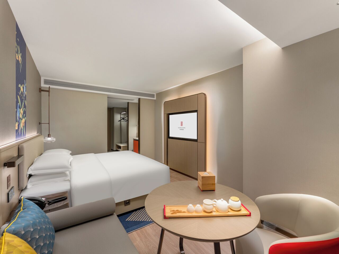 Habitación de hotel con cama, mesita de noche con juego de té, una silla y una pantalla de televisión.