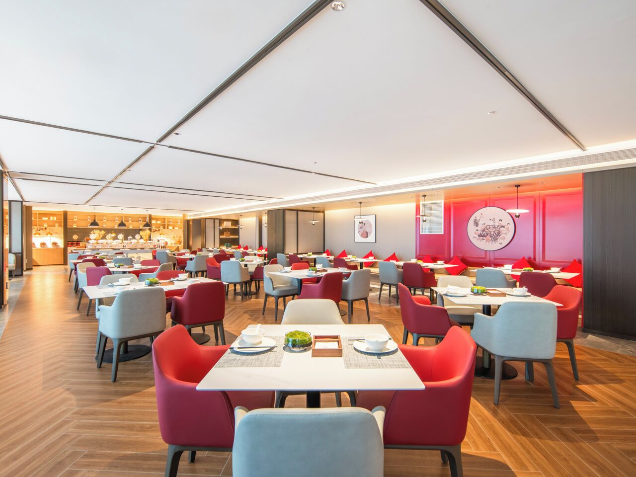Een ruime eetruimte met meerdere tafels en stoelen, een centrale doorgang en een zichtbare keuken in de achtergrond.