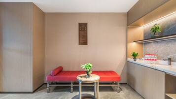 A compact room with a red sofa, a small round table with a plant, and a kitchen area with a marble countertop.