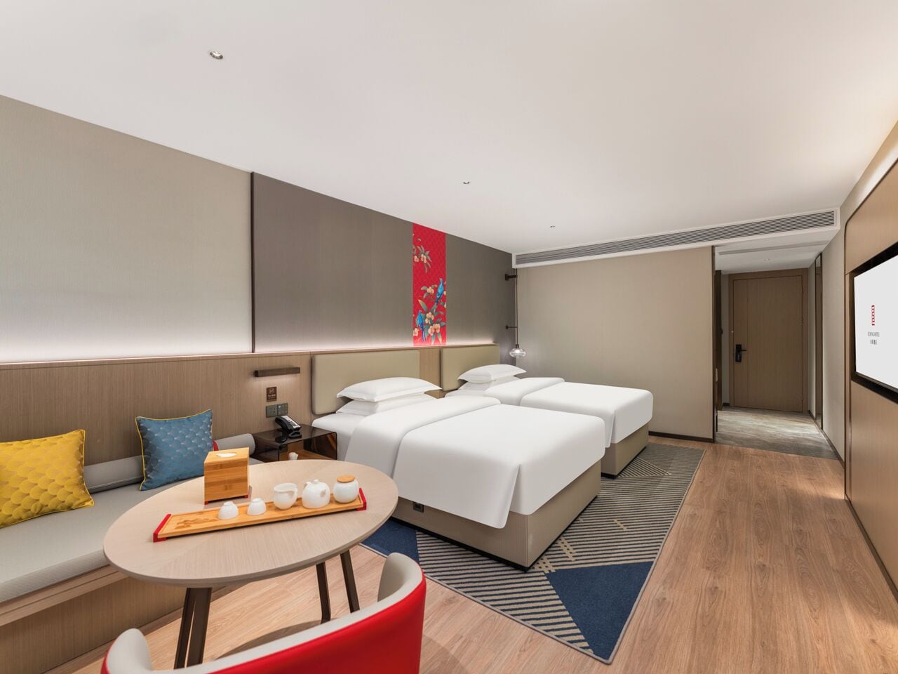 A modern hotel room with a sofa, a bed with white linens, a small table with tea set, and a colorful artwork on the wall.