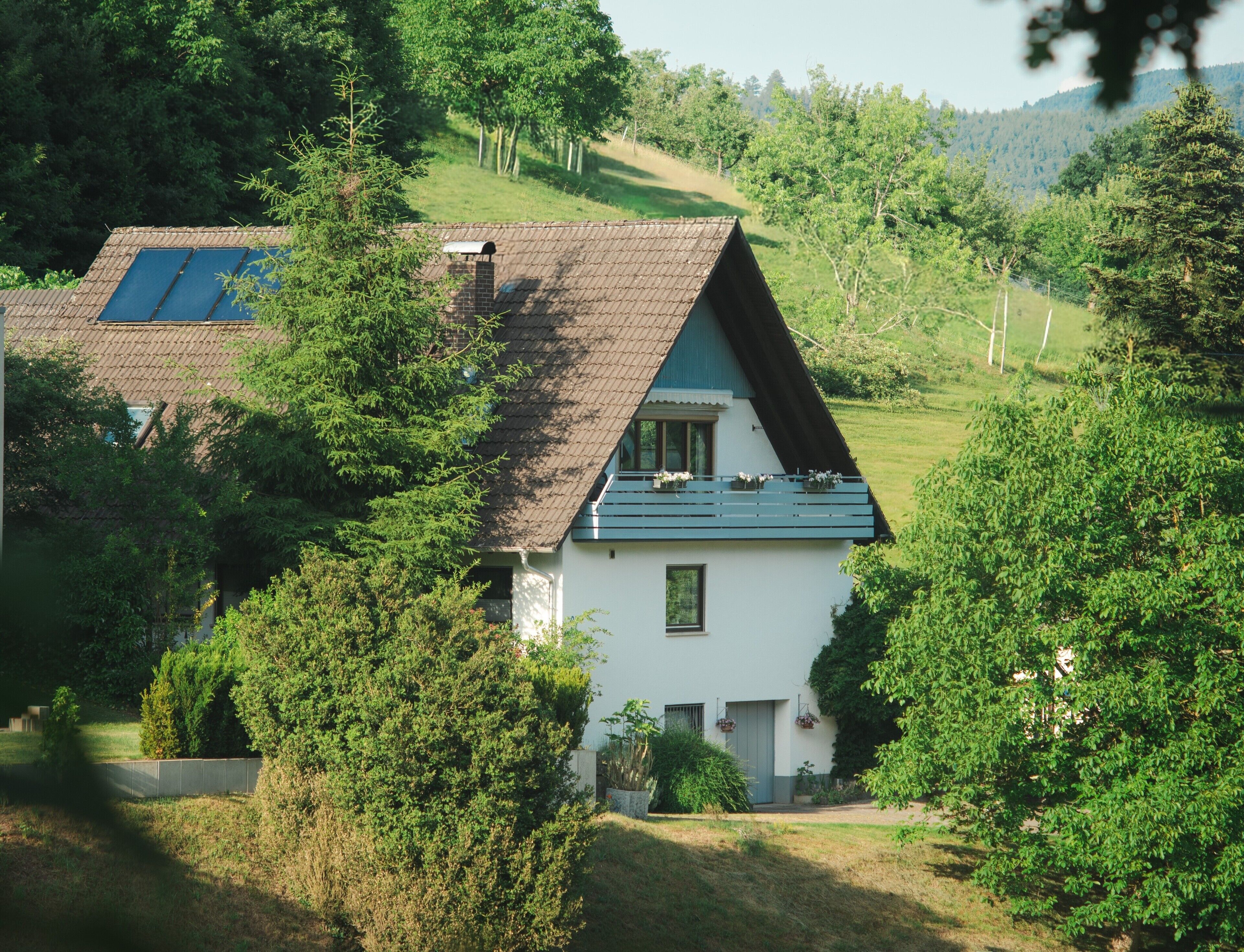 Una casa con techo inclinado, un balcón con plantas en macetas y un panel solar en el tejado.