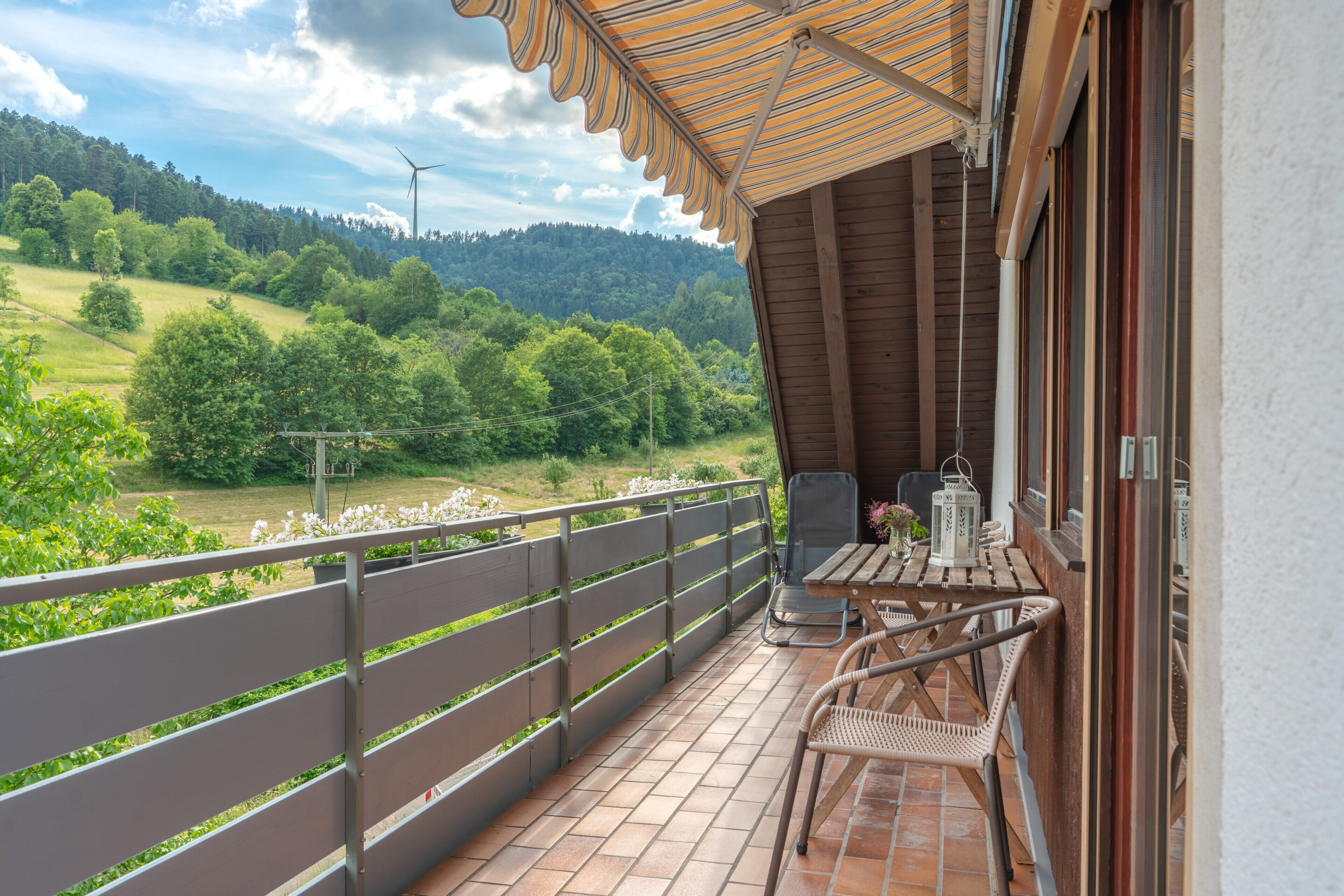 Ein Balkon mit Blick auf eine grüne Landschaft, ein Tisch mit Stühlen und einem Hängesessel.