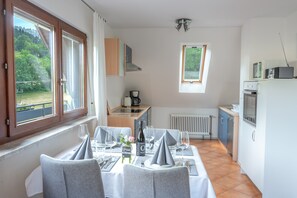 A dining area with a table set for four, a kitchen in the background, and a view of greenery outside. - Apartment 'Wolter' with Shared Terrace, Garden, and Wi-Fi (Gengenbach)