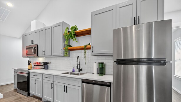 Una cocina moderna con electrodomésticos de acero inoxidable, armarios grises y una repisa de madera con plantas.