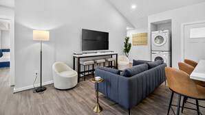 Una sala moderna con sofá, sillas, televisor, mesa de centro y lavadora.