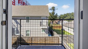 Un balcón con vista a una zona residencial, que incluye una casa con detalles rojos y una valla.