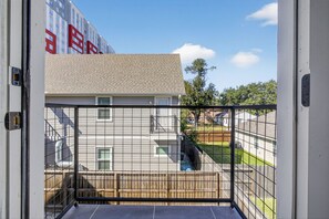 Ein Balkon mit Blick auf eine Wohngegend, darunter ein Haus mit rotem Akzent und ein Zaun.