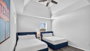 Una habitación con dos camas, un ventilador de techo, una ventana con vista a edificios y una pared con un letrero.