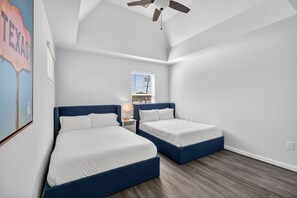 Ein Zimmer mit zwei Betten, einem Deckenventilator, einem Fenster mit Blick auf Gebäude und einer Wand mit einem Schild.