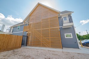 A modern two-story house with a large garage door, a wooden fence, and a clear sky.