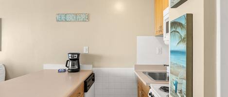 Una cocina compacta con cafetera, lavamanos y estufa.