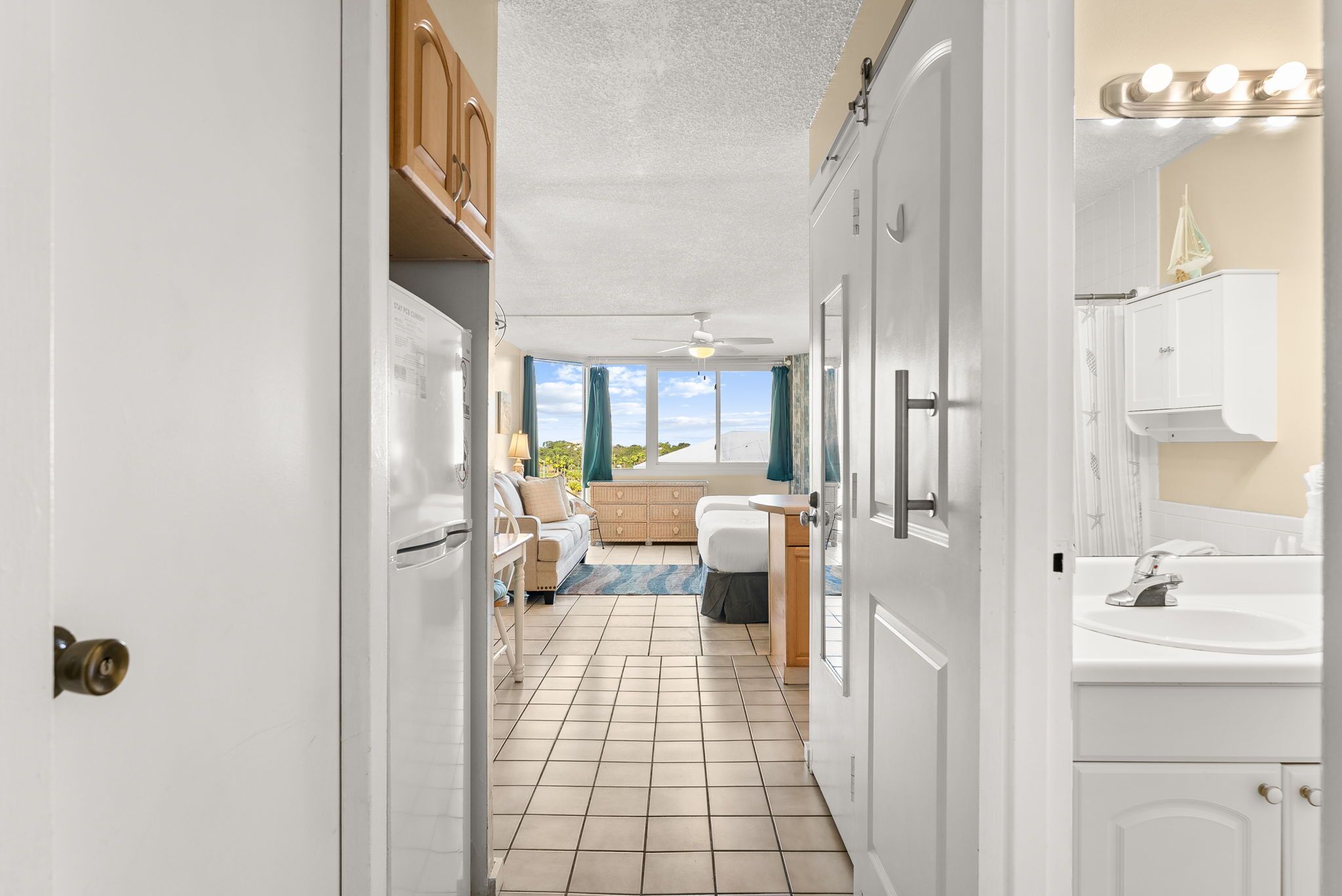 A narrow hallway leading to a bedroom with a large window, a ceiling fan, and a view of the outdoors.