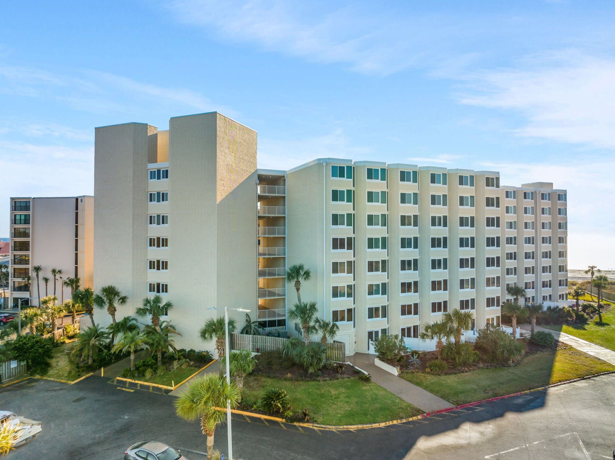 A multi-story hotel with a modern design, featuring a central courtyard with palm trees and a parking area.