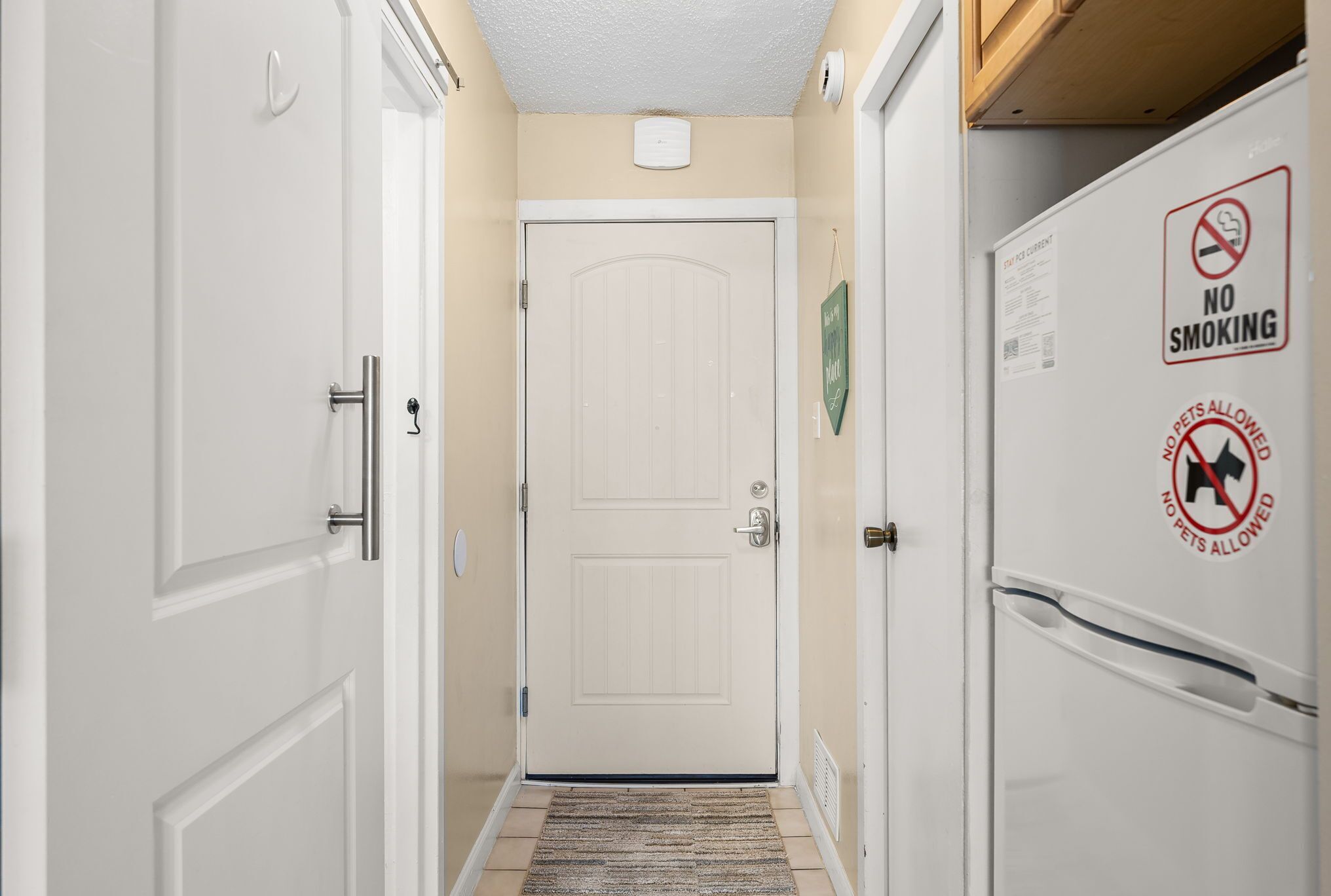 A hallway with a closed door, a no smoking sign, and a no pets allowed sign.