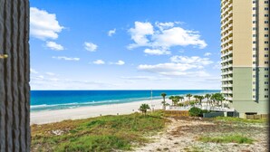 Blick auf einen Strand mit einem hohen Gebäude, einer sandigen Fläche mit Gras und blauem Himmel.