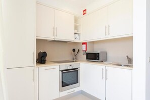 A compact kitchen with white cabinets, a microwave, a coffee maker, and a stove. - Snazzy Varandas do Castelo One Bedroom Apartment Sleeps 2 Persons (Albufeira)