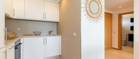 A modern kitchen with white cabinets, a built-in oven, and a countertop with a sink and a decorative mirror.