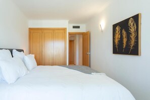 A bedroom with a large bed, wooden wardrobe, and a wall-mounted artwork. - Snazzy Varandas do Castelo One Bedroom Apartment Sleeps 2 Persons (Albufeira)