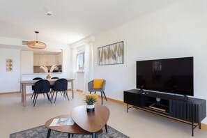A modern living room with a flat-screen TV, a dining area with a table and chairs, and a kitchen visible in the background. - Snazzy Varandas do Castelo One Bedroom Apartment Sleeps 2 Persons (Albufeira)