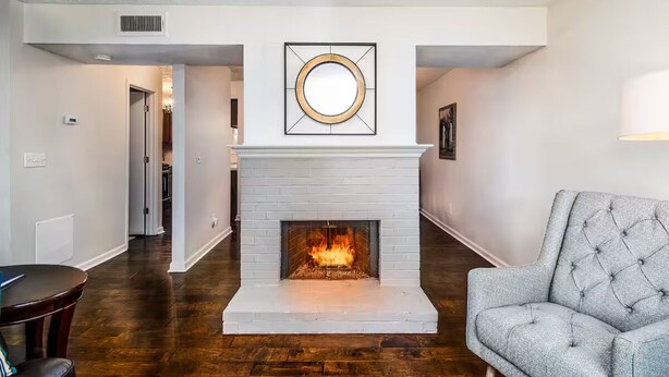 A living room with a fireplace, a grey armchair, and a hallway leading to another room.