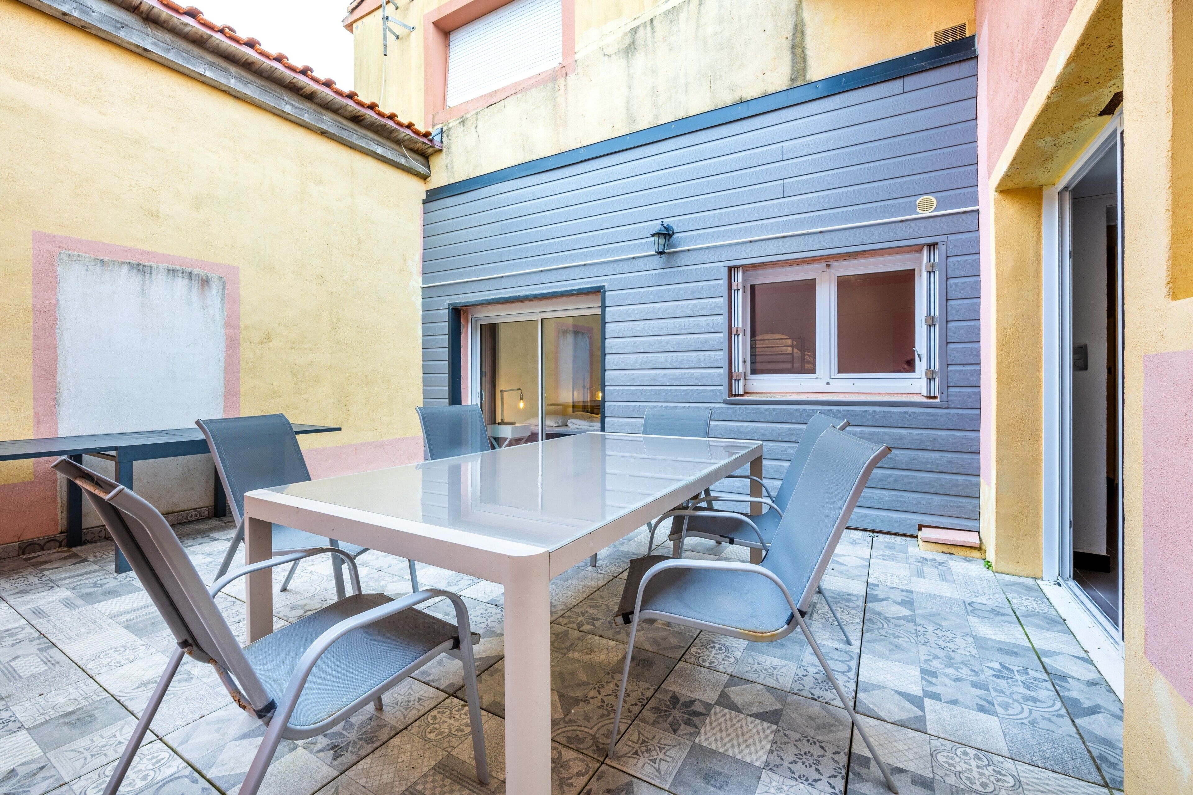 Eine Außenpatio mit Tisch und Stühlen, ein Fliesenboden und ein Gebäude mit blauer Außenwand.
