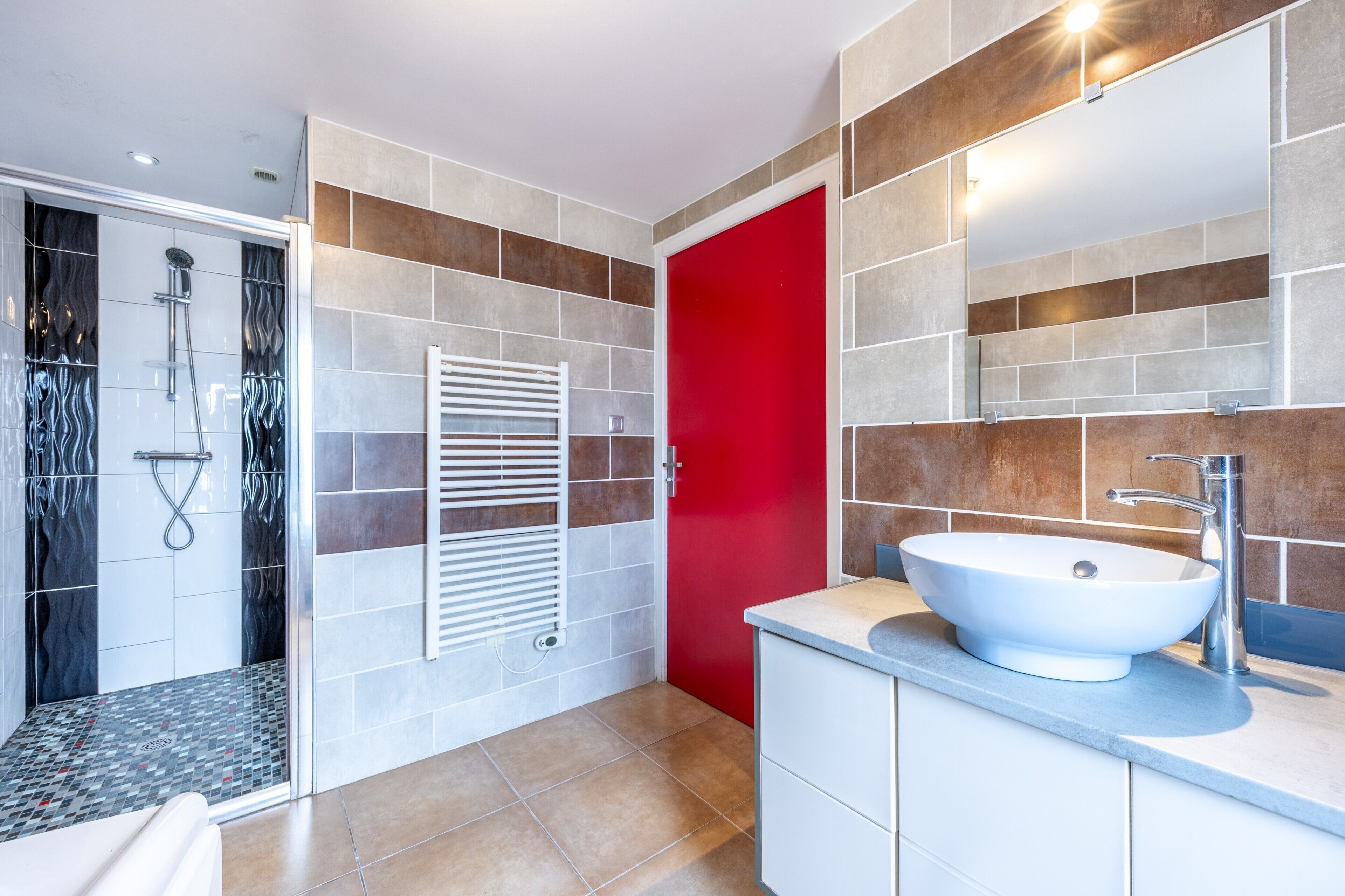 Un baño moderno con ducha, una puerta roja y un lavamanos blanco.