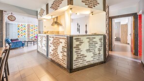 A kitchen area with a brick accent wall, a clock, and a dining area with a blue sofa. - Holiday Home 'Sleeps 22 Brem Center with Large' (Brem-sur-Mer)