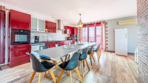 A modern kitchen with red cabinets, a long dining table, and black chairs. - Holiday Home 'Sleeps 22 Brem Center with Large' (Brem-sur-Mer)