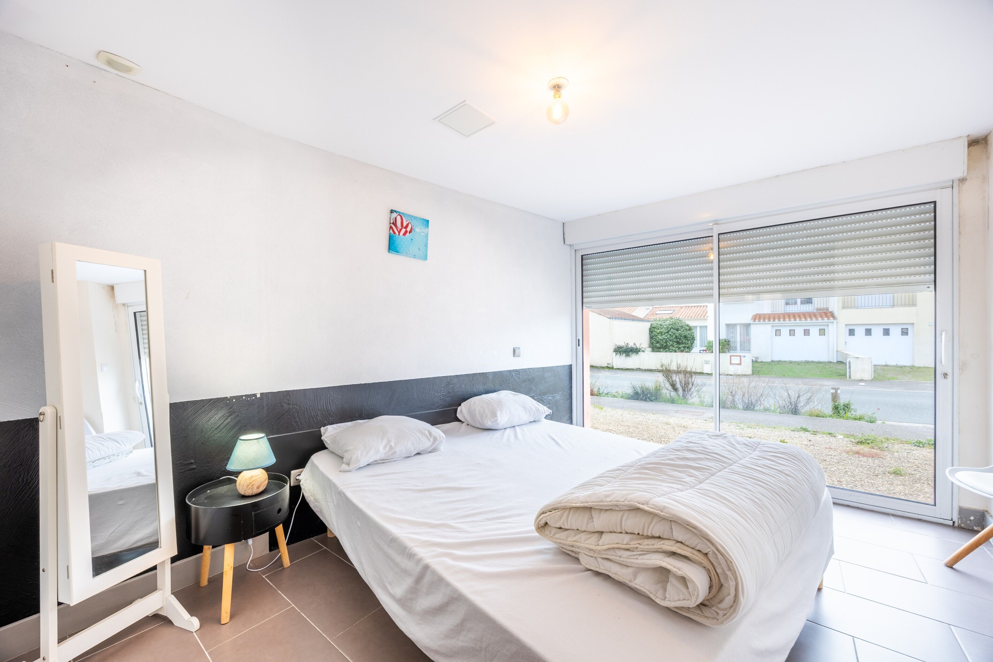 Une chambre d’hôtel avec un lit, une table de chevet avec une lampe, un miroir et une vue sur l’extérieur par une grande fenêtre.