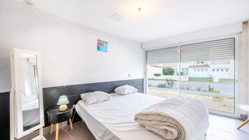 Une chambre d’hôtel avec un lit, une table de chevet avec une lampe, un miroir et une vue sur l’extérieur par une grande fenêtre.