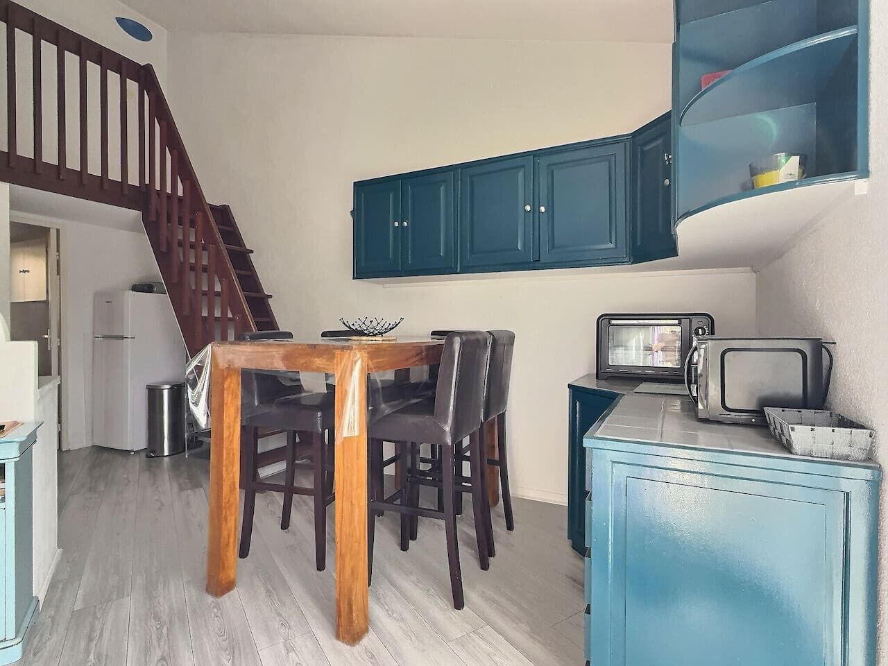 A compact kitchen with a dining table, chairs, a microwave, and a blue cabinet.
