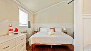 Ein Schlafzimmer mit einem hölzernen Bett, weißer Bettwäsche, einer Kommode mit Schubladen, einem Fenster mit Jalousien und einem Wandheizkörper.