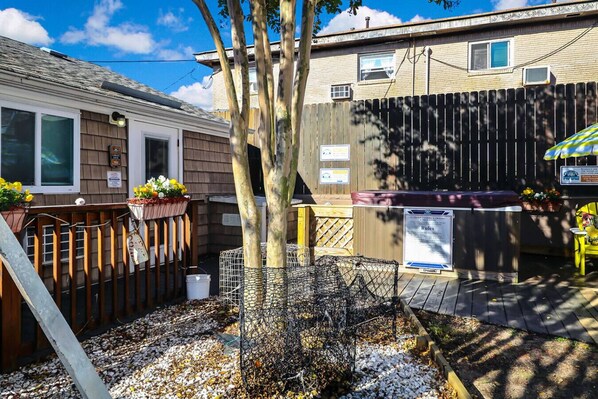 Un jardin à l’arrière d’une maison, avec une clôture en bois, un arbre, une mangeoire à oiseaux et un barbecue.
