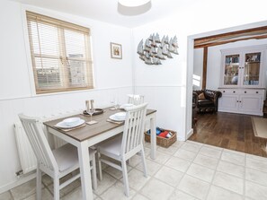 A dining area with a wooden table and white chairs, a white cabinet with glass doors, and a fish wall decoration. - Sheepwash Barn (Freshwater)