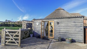 A rustic wooden building with a thatched roof, a stone wall, and a wooden gate. - Sheepwash Barn (Freshwater)