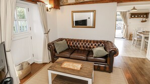 A cozy living room with a brown leather sofa, a white coffee table, and a stone wall. - Sheepwash Barn (Freshwater)